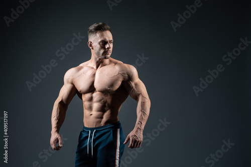 young handsome sportsman bodybuilder posing on dark background © goami