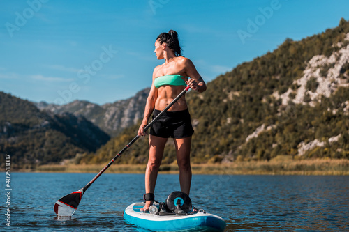 Young athletic woman rowing on a SUP stand up paddle board in a river on a hot summer day