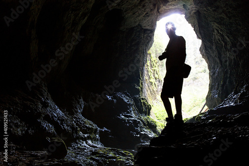 Tourist in the Occidental Carpathians, Radesei Cave, Romania. Entrance to the cave, the silhouette of a man against the sky, a huge hole in the rock, see from the cave photo