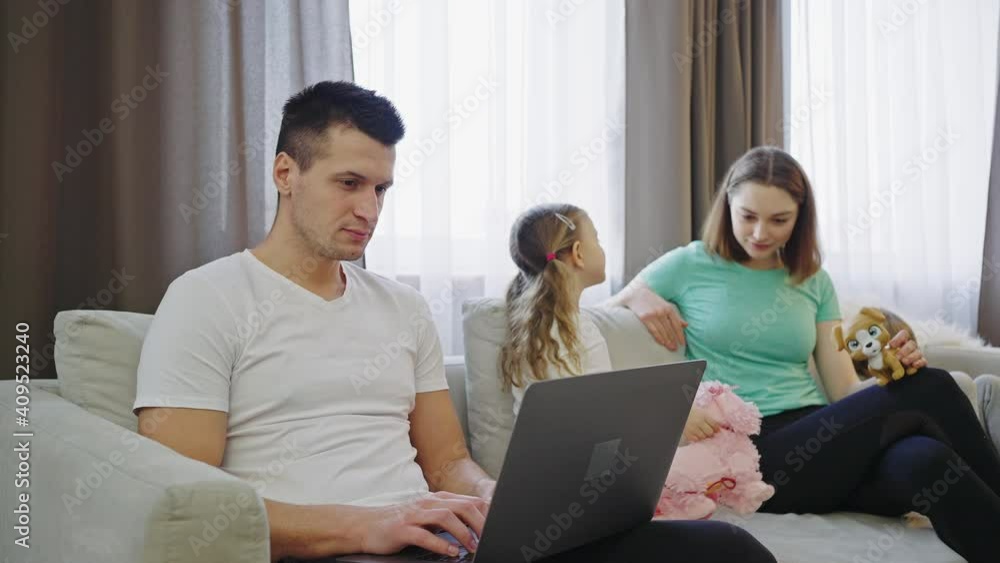 Father working on laptop, his wife, daughter and son playing toys nearby, slow motion Father working on laptop, his wife, daughter and son playing toys nearby, slow motion