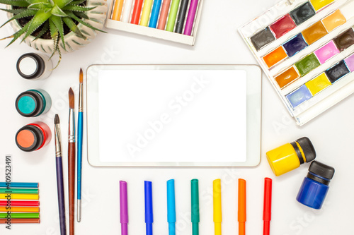 White digital tablet with a blank screen on a white table and drawing supplies