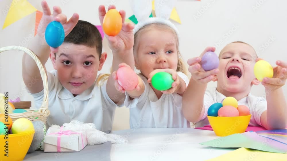 Funny kids in bunny ears draws eggs for Easter day. Children eat sweets and laugh. Funny kids in bunny ears draws eggs for Easter day. Children eat sweets and laugh.