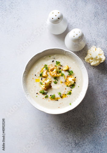 Cheesy cauliflower soup in white bowl on gray stone background close up