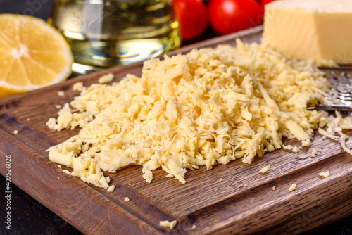 Fresh hard cheese grated on a large grater on a wooden cutting board