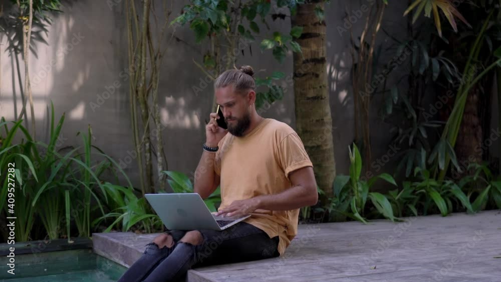 Caucasian male in casual wear using laptop computer for remote job at pool terrace talking on smartphone, skilled man making cellular call using roaming connection during distance job Caucasian male in casual wear using laptop computer for remote job at pool terrace talking on smartphone, skilled man making cellular call using roaming connection during distance job