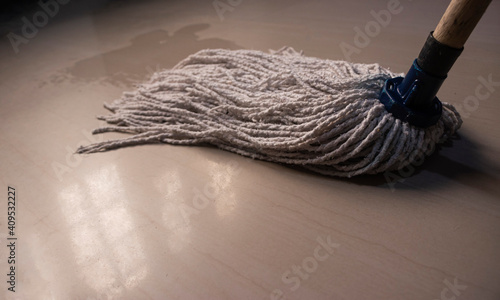 Fotografia A white mop cleaning a beige floor with a blue handle and liquid on the floor, i