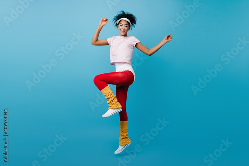 Fototapeta Naklejka Na Ścianę i Meble -  Graceful black girl doing aerobics. Gorgeous african woman jumping on blue background.
