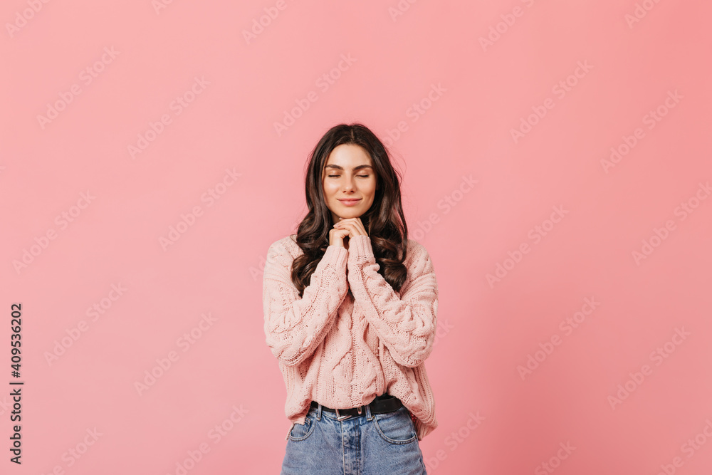 Curly brunette calmly smiles with closed eyes on pink background and makes wish Curly brunette calmly smiles with closed eyes on pink background and makes wish