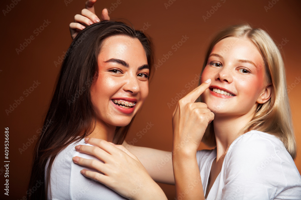 two pretty diverse girls happy posing together: blond and brunette, caucasian and asian on brown background, lifestyle people concept two pretty diverse girls happy posing together: blond and brunette, caucasian and asian on brown background, lifestyle people concept