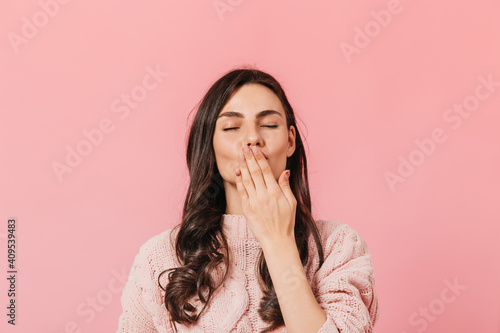 Close-up shot of dark-haired lady in light sweater blowing air kiss on pink background