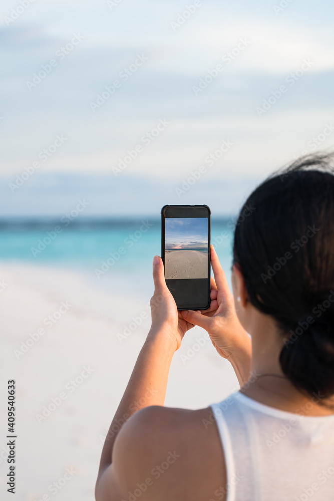 a woman capturing the pristine white sand beach using her smart phone