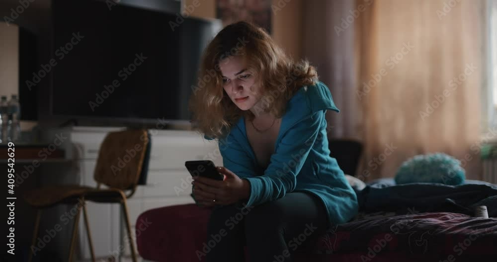 Beautiful woman using mobile phone sitting on bed alone at home Beautiful woman using mobile phone sitting on bed alone at home