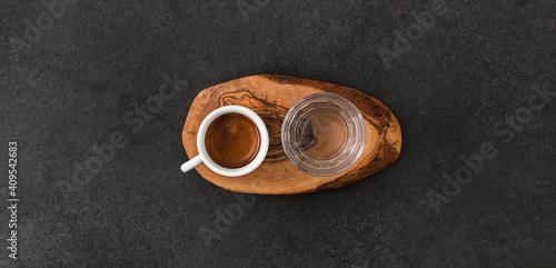 Cup of espresso coffee and glass on wooden pad on dark table, speciality coffee serving concept. Top view.