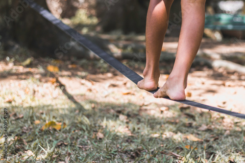 Close up on feet walking on tightrope or slackline outdoor in a city park in back light - slacklining, balance, training concept