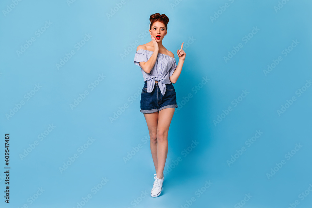 Stunning pinup woman pointing up with finger. Full length view of surprised ginger lady wears denim shorts. Stunning pinup woman pointing up with finger. Full length view of surprised ginger lady wears denim shorts.