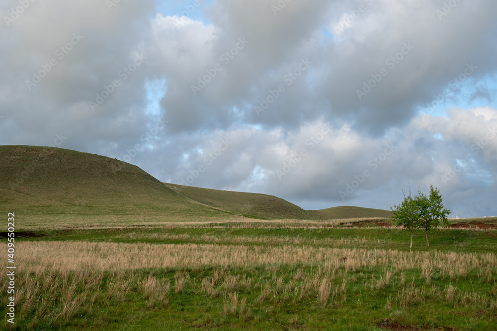 Hilly area covered with green grass. Very beautiful, cloudy sky. There is free space for insertion.