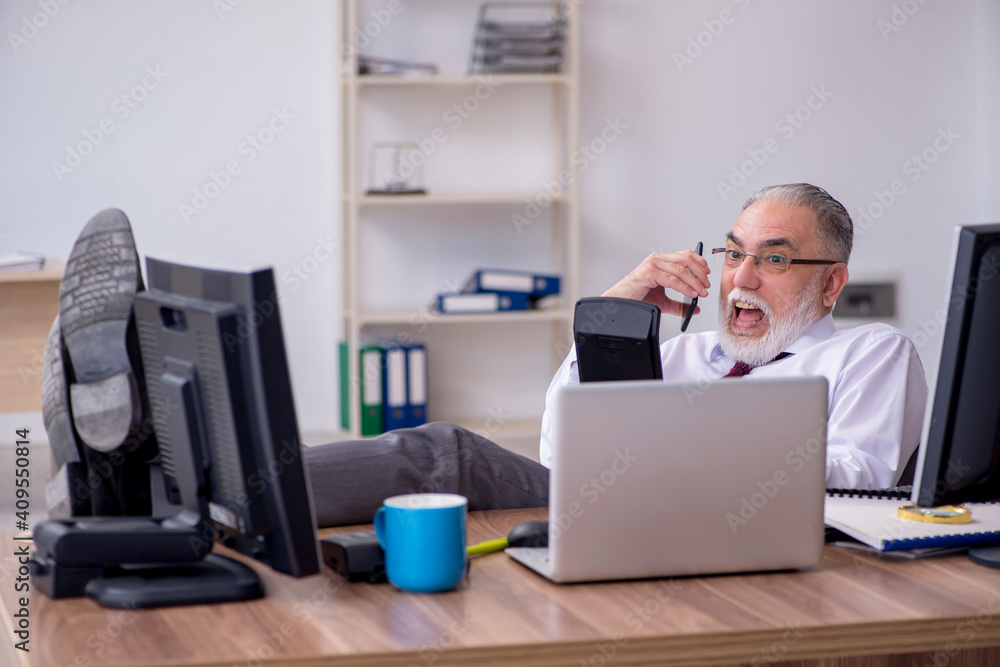 Old male boss sitting at desktop in the office Old male boss sitting at desktop in the office