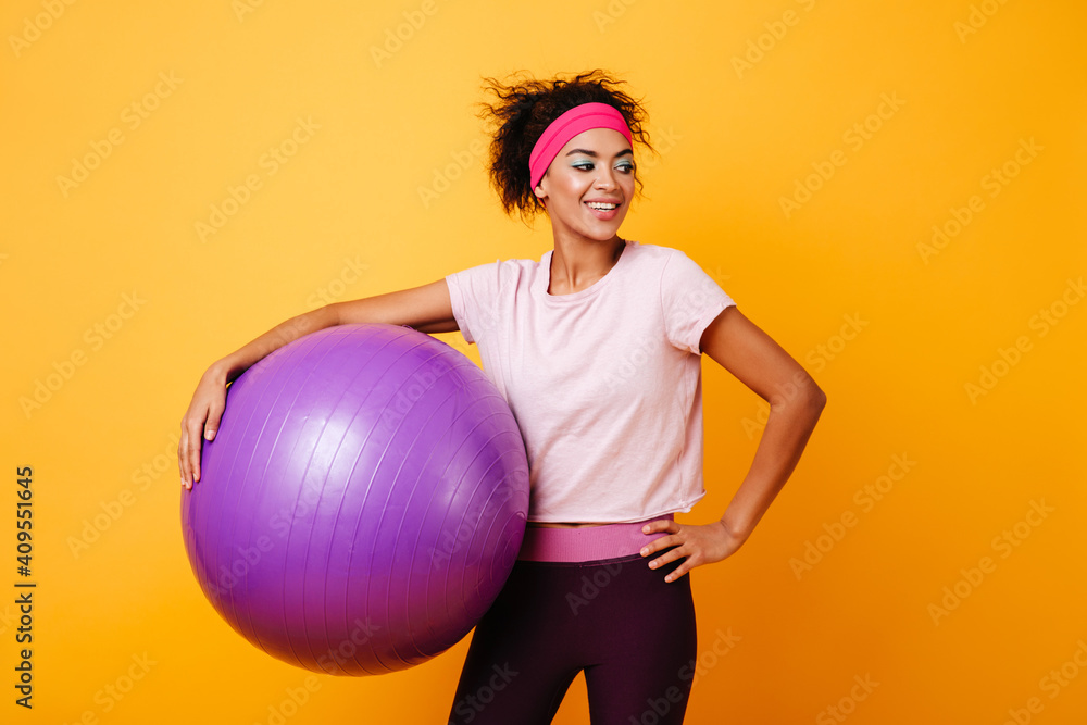 Inspired african girl posing after training on yellow background. Happy african woman holding fitness ball. Inspired african girl posing after training on yellow background. Happy african woman holding fitness ball.