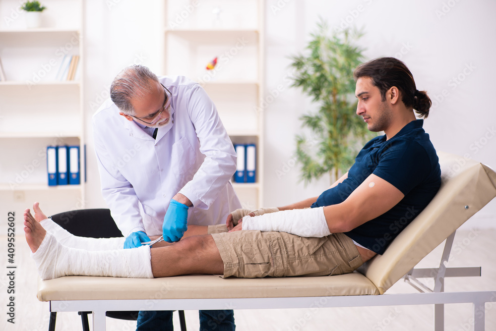 Young injured man visiting old doctor traumatologist Young injured man visiting old doctor traumatologist