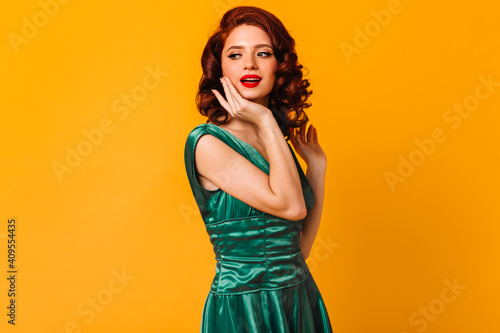 Magnificent young woman in green dress looking away. Studio shot of dreamy girl isolated on yellow background.