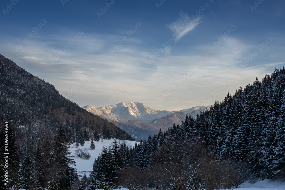 Snow covered hilly landscape in the evening.Mountain peaks in the background.