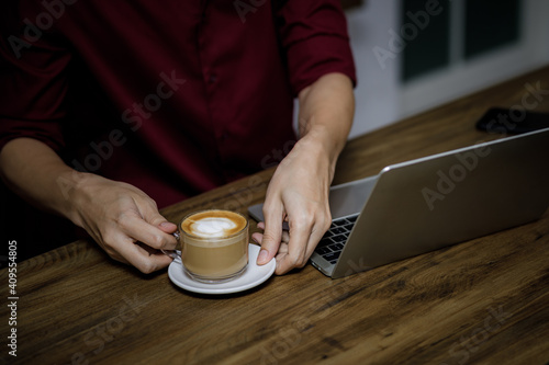 asian freelancer holding cup of coffee at workplace and laptop on the table in cafe