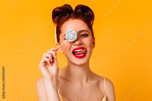 Playful caucasian woman holding lollipop. Gorgeous red-haired girl posing with hard candy.