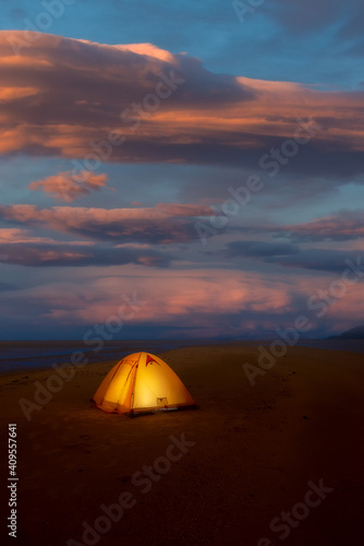 The tent lights up inside. Take image in the atmosphere that there is sunlight with clouds in the background.