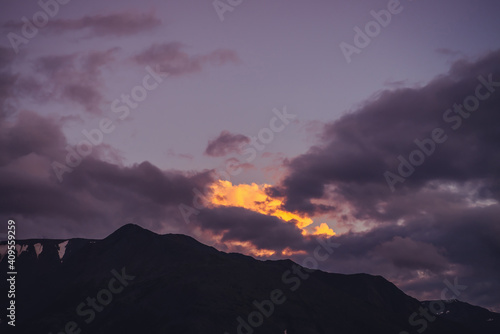 Atmospheric mountain scenery with lilac dawn sky. Scenic landscape with rocks with snow under purple sunset sky. Beautiful sunrise in mountains in pastel tones. Illuminating color in dawn cloudy sky.