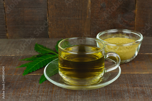 Neem tea in transparent glass cup and fresh neem leaf on wooden background.