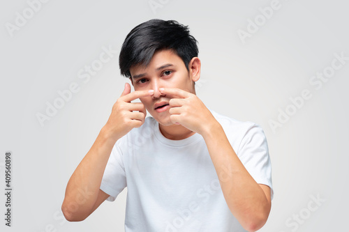 A young Asian man squeezes a pimple on the tip of his nose.