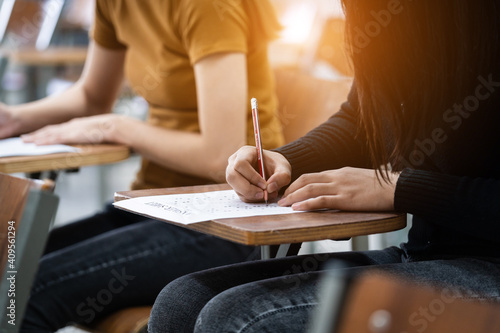 Young female university students concentrate on doing examinations in the classroom. Girl students seriously write the exercise of the examinations in the classroom. photo