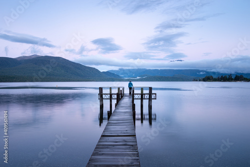 Lonely woman standing at the end of Lake Te Anau jetty at sunrise, looking at the Kepler mountains. Landscape format.