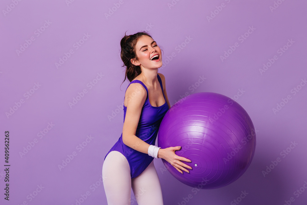 Beautiful girl in purple bodysuit and leggings does exercises with huge fitball on isolated background Beautiful girl in purple bodysuit and leggings does exercises with huge fitball on isolated background