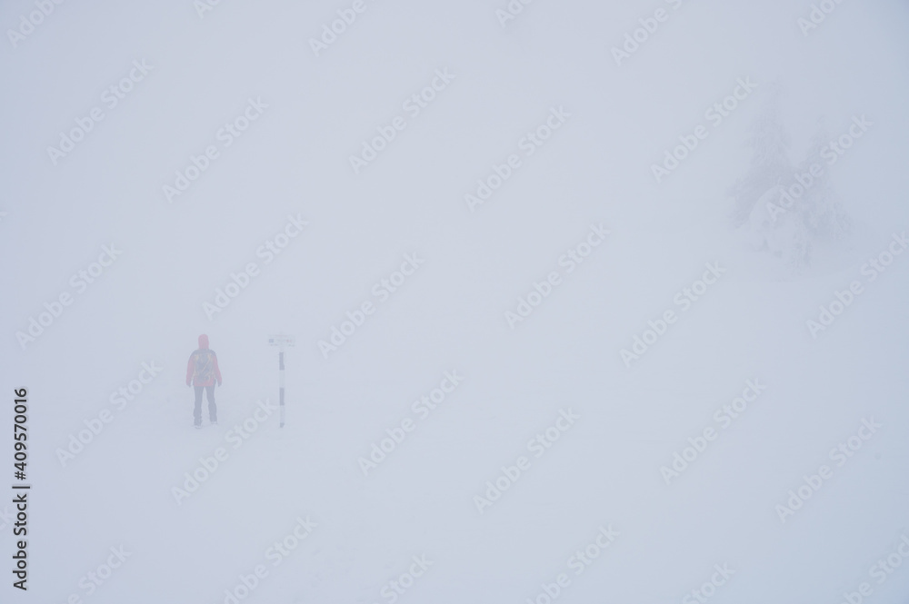 Hiker on a trail in Romanian Carpathian mountains with reduced visibility due to fog and snow