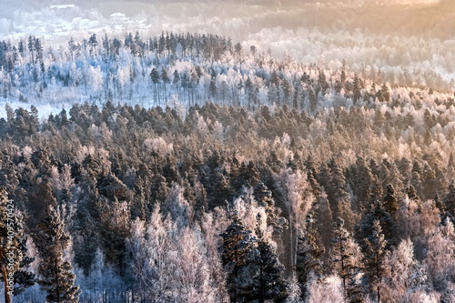 Winter landscape with forest, mountains, frosty haze in the rays of the setting sun