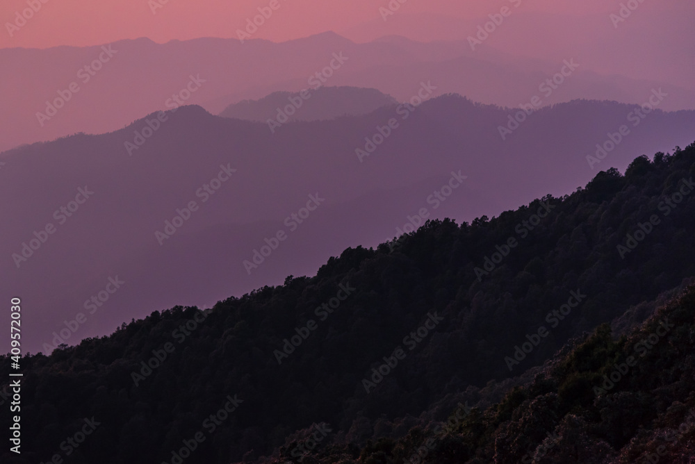 View of Himalayas mountain range with visible silhouettes through the colorful fog from Binsar Zero point trek trail in  himalayan region of Kumaon, Uttarakhand, India.