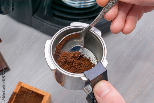 a person makes coffee in a coffee machine pours ground coffee into the dispenser with a spoon