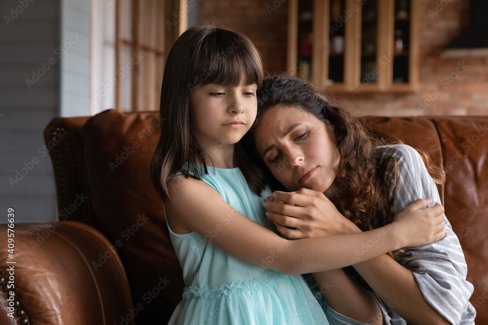 Close up caring little girl comforting, hugging depressed mother, sitting on couch at home, preschool daughter calming, embracing upset frustrated mum, family overcoming problems together, divorce Close up caring little girl comforting, hugging depressed mother, sitting on couch at home, preschool daughter calming, embracing upset frustrated mum, family overcoming problems together, divorce