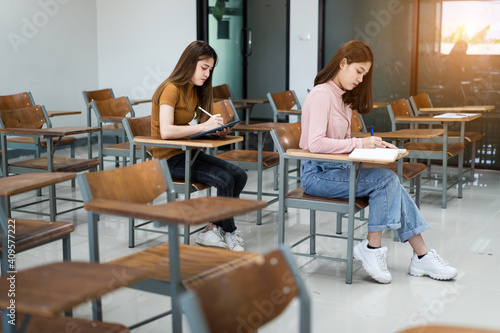 Selective focus of the teen college students sitting on lecture chair in classroom write on examination paper answer sheet in doing the final examination test. Female students in the student uniform.