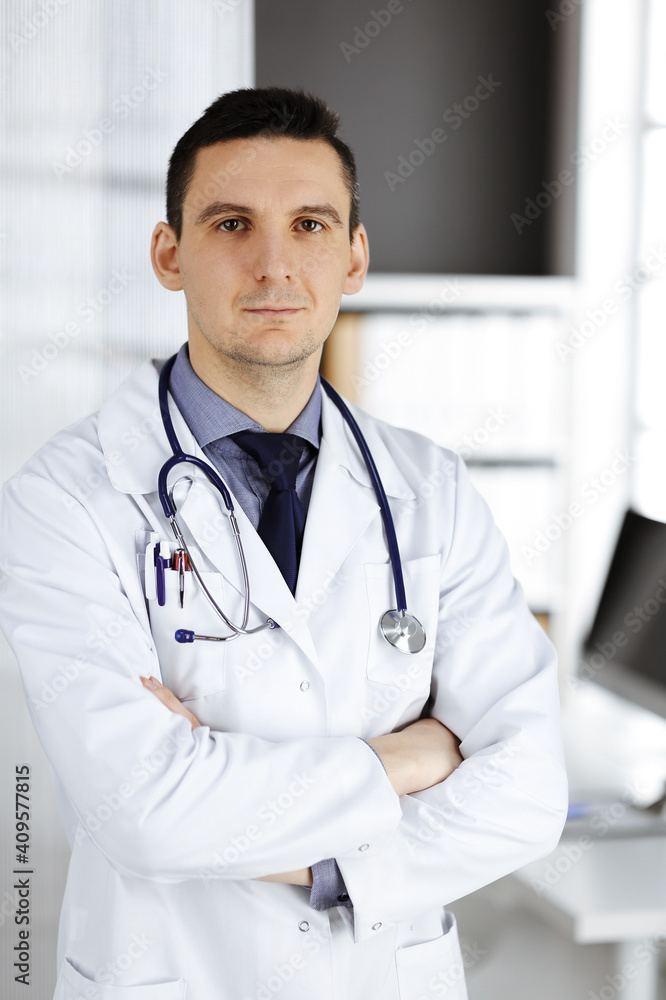 Male doctor standing straight with arms crossed in clinic near his working place. Perfect medical service in hospital. Medicine and healthcare concept Male doctor standing straight with arms crossed in clinic near his working place. Perfect medical service in hospital. Medicine and healthcare concept