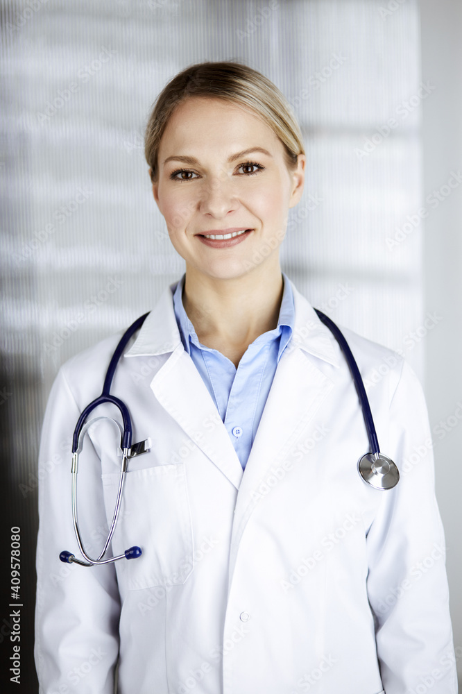 Friendly female doctor standing in clinic. Portrait of cheerful smiling physician. Perfect medical service in hospital. Medicine and healthcare concept Friendly female doctor standing in clinic. Portrait of cheerful smiling physician. Perfect medical service in hospital. Medicine and healthcare concept