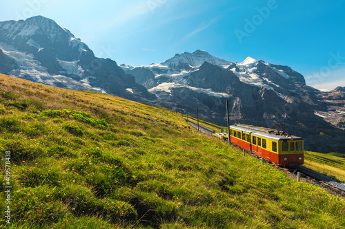 Electric retro tourist train and snowy mountains in background, Switzerland