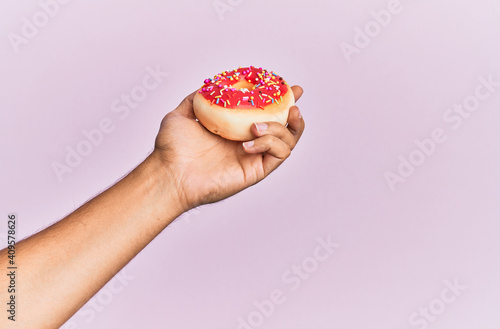Hand of hispanic man holding donut over isolated pink background.