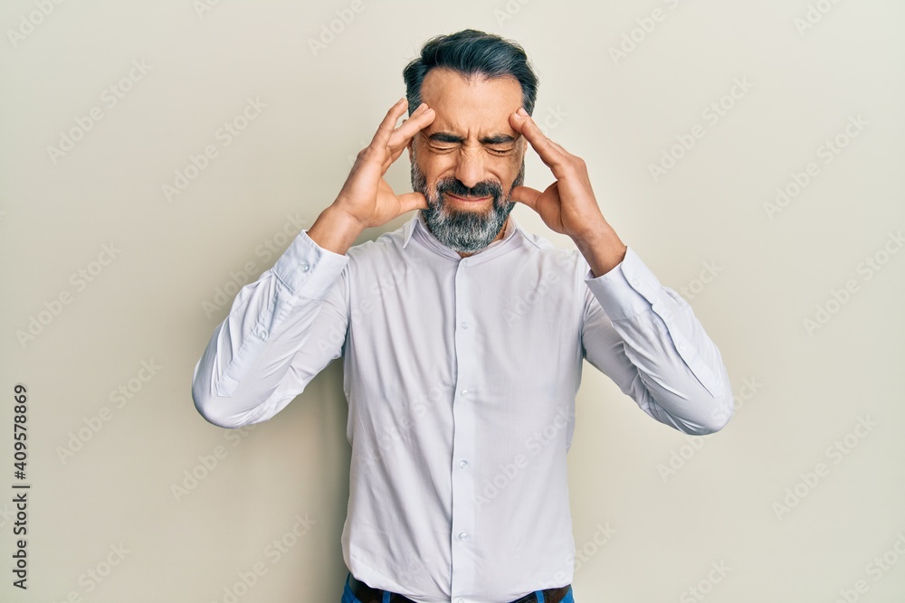 Middle age man with beard and grey hair wearing casual white shirt with hand on head, headache because stress. suffering migraine. Middle age man with beard and grey hair wearing casual white shirt with hand on head, headache because stress. suffering migraine.