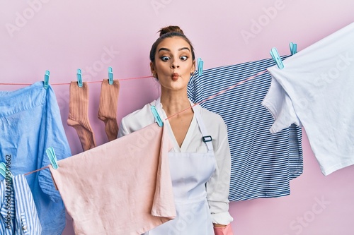 Beautiful brunette young woman washing clothes at clothesline making fish face with lips, crazy and comical gesture. funny expression.
