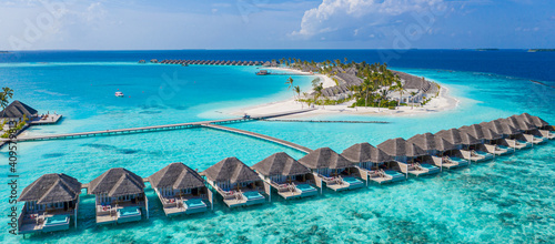 Aerial view of Maldives island, luxury water villas resort and wooden pier. Beautiful sky and ocean lagoon beach background. Summer vacation holiday and travel concept. Paradise aerial landscape pano © icemanphotos