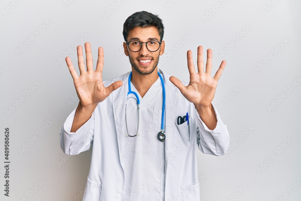 Young handsome man wearing doctor uniform and stethoscope showing and pointing up with fingers number ten while smiling confident and happy. Young handsome man wearing doctor uniform and stethoscope showing and pointing up with fingers number ten while smiling confident and happy.