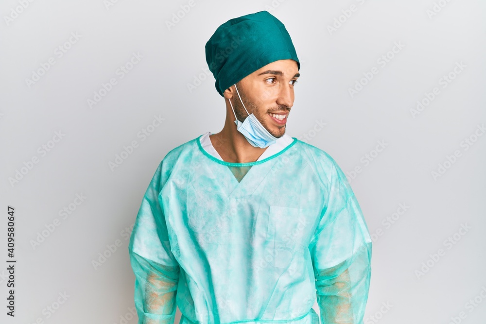 Young handsome man wearing surgeon uniform and medical mask looking to side, relax profile pose with natural face and confident smile. Young handsome man wearing surgeon uniform and medical mask looking to side, relax profile pose with natural face and confident smile.