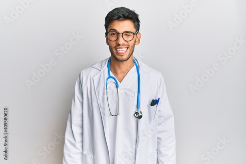 Young handsome man wearing doctor uniform and stethoscope winking looking at the camera with sexy expression  cheerful and happy face.